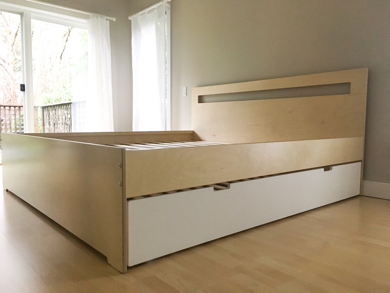 May include: A light wood platform bed frame with a white drawer underneath. The headboard has a rectangular cutout in the top.