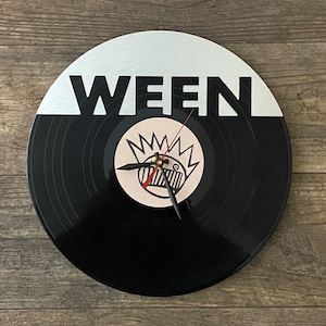 May include: A black vinyl record clock with a white face and the word "WEEN" printed in black letters. The clock face features a cartoon character with a crown of teeth.
