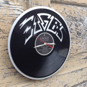 May include: A black vinyl record clock featuring the Eagles band logo and album title "The Long Run". The clock hands are silver and red.