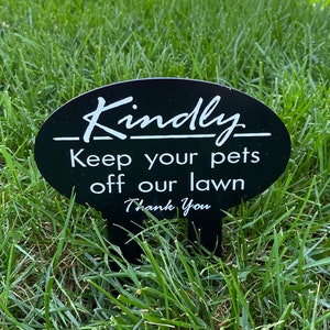 May include: Black and white sign with the text "Kindly Keep your pets off our lawn Thank You" on a green grassy lawn.