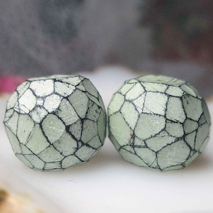 May include: A set of three ceramic mugs with a speckled, cream-colored glaze. Each mug features a different hand-painted floral design in shades of blue, green, and yellow. The mugs have a simple, rounded shape and a comfortable handle.