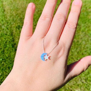 May include: A silver chain necklace with a blue and white opal crescent moon and star pendant.
