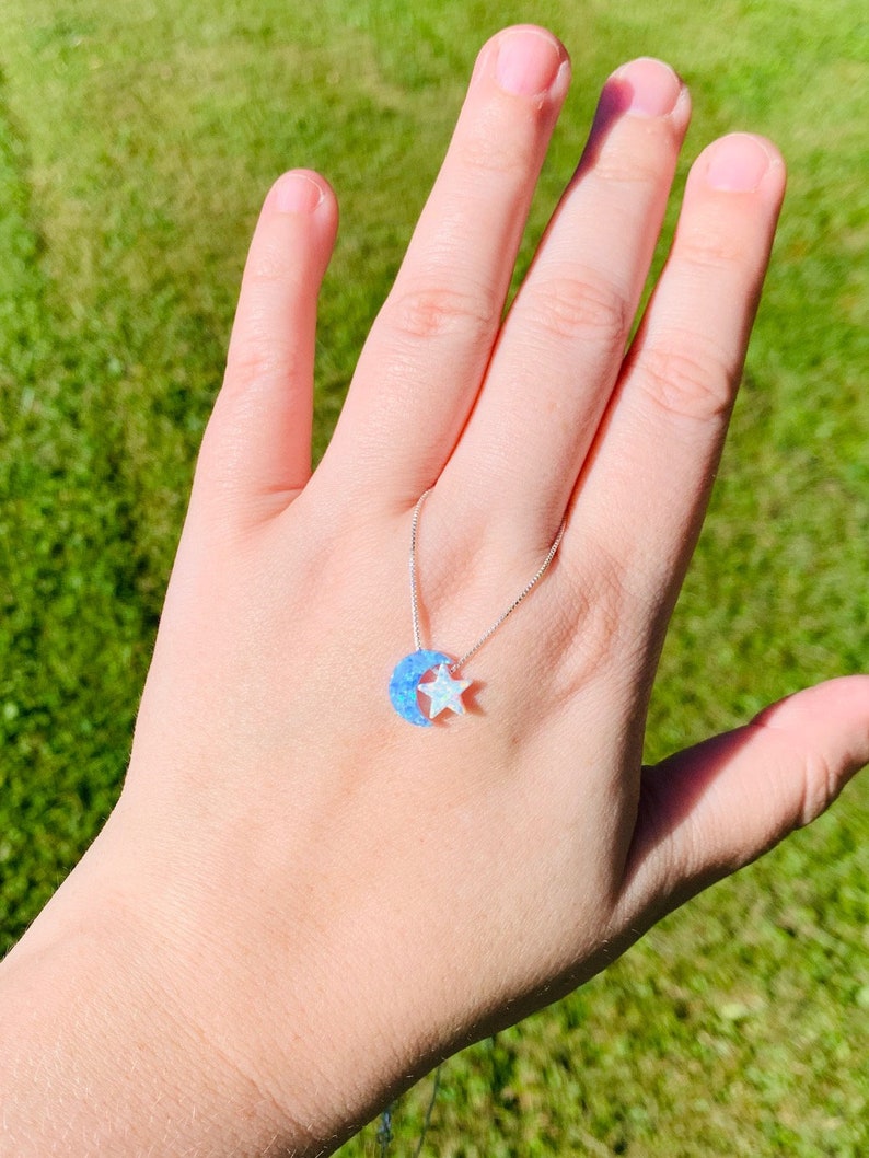 May include: A silver chain necklace with a blue and white opal crescent moon and star pendant.