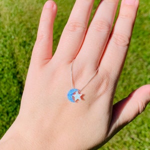 May include: A silver chain necklace with a blue and white opal crescent moon and star pendant.
