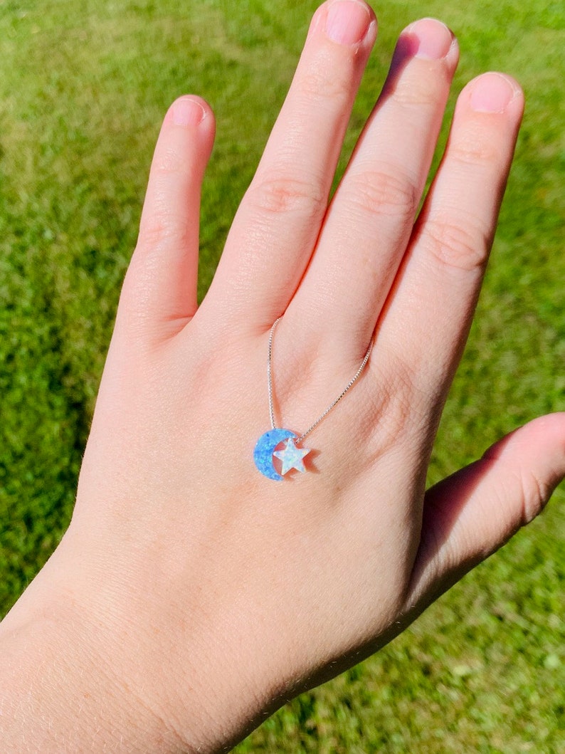 May include: A silver chain necklace with a blue and white opal crescent moon and star pendant.