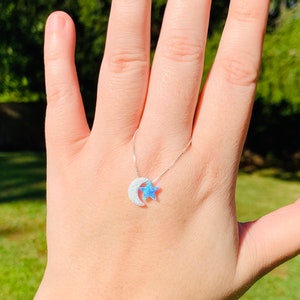 May include: A silver chain necklace with a crescent moon and star pendant. The moon and star are made of white opal with a blue iridescent sheen.