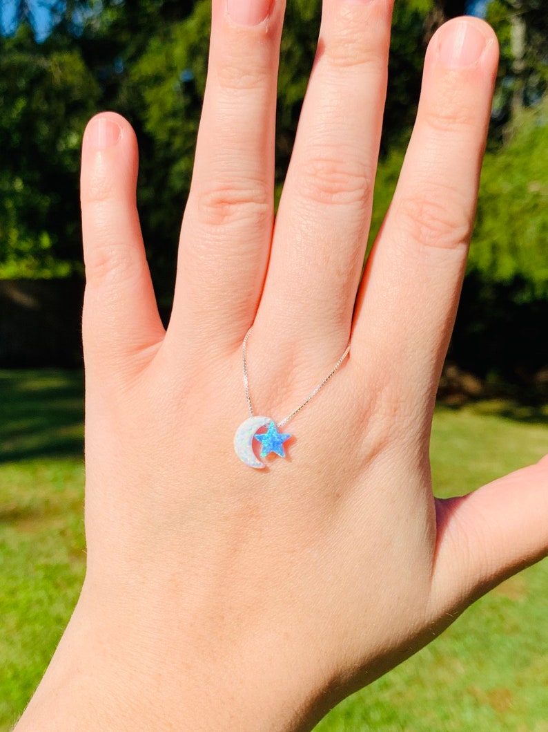 May include: A silver chain necklace with a crescent moon and star pendant. The moon and star are made of white opal with a blue iridescent sheen.