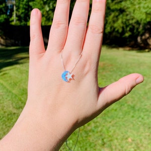 May include: A silver chain necklace with a crescent moon and star charm. The moon is made of blue opal and the star is white.