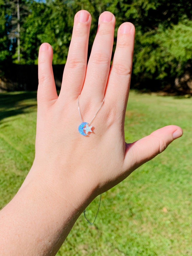 May include: A silver chain necklace with a crescent moon and star charm. The moon is made of blue opal and the star is white.