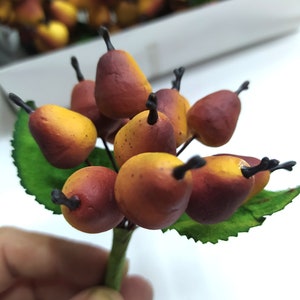 Può includere: Un mazzo di bacche finte con una miscela di toni marroni e gialli. Le bacche sono attaccate a uno stelo verde con foglie.