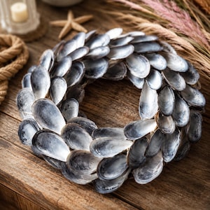 Peut inclure: Une couronne circulaire composée de nombreuses coquilles de moules gris foncé et argentées qui se chevauchent. Les coquilles sont disposées en un motif dense et superposé, créant une forme arrondie et texturée avec un centre creux.
