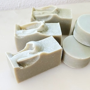 May include: Four bars of green soap, three are rectangular and one is round. The rectangular bars have a textured surface and the round bar is smooth.