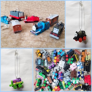 May include: A collection of toy train keychains and pendants in various colors. The keychains feature different train designs, including blue, red, and brown locomotives. Some pendants are attached to silver chains. A variety of miniature train toys are also visible.