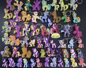 Könnte beinhalten: Eine Sammlung kleiner Pony-Figuren aus Kunststoff, von denen viele an Metallschlüsselanhängern befestigt sind. Die Figuren haben verschiedene Farben wie Rosa, Blau, Gelb, Grün und Lila. Einige Ponys sind mit violetten X-Symbolen markiert.