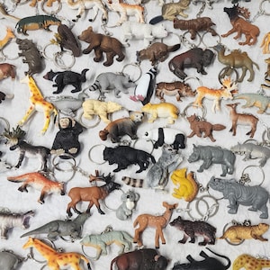 Pode incluir: Uma coleção de chaveiros em forma de animais, incluindo ursos, girafas, rinocerontes e pandas. Os chaveiros são feitos de plástico e apresentam argolas prateadas. Os animais são de várias cores, como castanho, cinzento e branco.