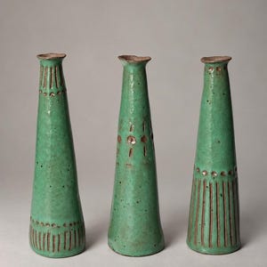 May include: Three tall, slender ceramic vases with a vibrant green glaze and a speckled texture. Each vase features a narrow neck and a flared base, decorated with incised vertical lines and small circular indentations in a dark brown tone.