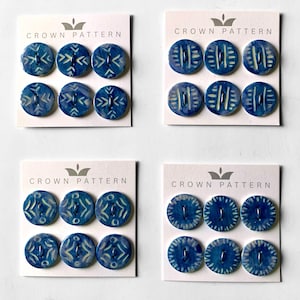 May include: Four sets of decorative blue ceramic buttons with white patterns. Each set contains six buttons on a white card. The cards are labeled "CROWN PATTERN" above the buttons. The buttons have different designs, including arrows, lines, and circles.