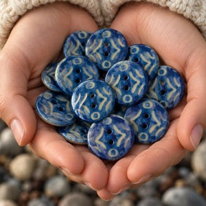 May include: A collection of round, two-hole buttons featuring a deep blue glaze with a contrasting cream-colored geometric pattern. Each button has a smooth, glossy finish and a circular shape, showcasing a consistent decorative motif throughout.