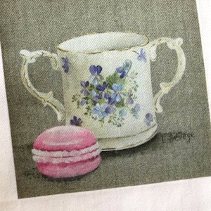 Peut inclure: Une tasse à thé blanche avec un motif floral et un macaron rose sur un fond gris.