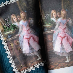 Peut inclure: Une impression encadrée de style vintage représentant deux filles en robes rose et bleue, debout devant un miroir. L'impression est encadrée d'une bordure en dentelle blanche et comporte un motif floral brodé dans le coin supérieur gauche.