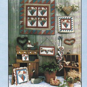 Op de afbeelding: Een display van handgemaakte quilts en decoratieve items met een landelijk thema. De quilts hebben geometrische patronen in rood, blauw en bruin. De afbeelding bevat de tekst "Broken Hearts" en "Country Threads".