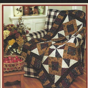 Peut inclure: Un livre de modèles de courtepointe intitulé My Best Thimbleberries Classic Country par Lynette Jensen, présentant une image de couverture d'une courtepointe en patchwork dans des tons marron, noir et blanc sur un fauteuil à carreaux.
