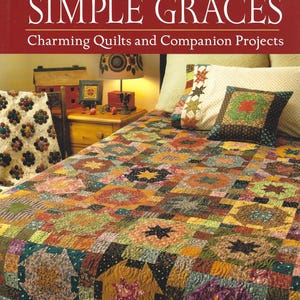 May include: A book cover titled Simple Graces by Kim Diehl featuring a bed covered in a multi-colored patchwork quilt with star motifs. The quilt displays various fabric patterns in shades of red, green, yellow, and brown. A matching pillow sits on the bed.