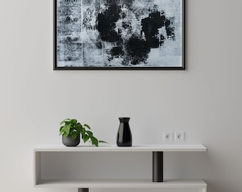 May include: A white shelf unit with two shelves, a black vase, and a potted plant. The shelf unit is against a white wall with a black framed abstract painting above it.
