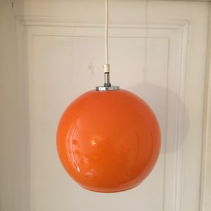 May include: A bright orange, round pendant light fixture hangs from a white cord. The light fixture is made of glass and has a chrome metal top.
