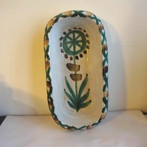 May include: A white ceramic dish with a green and brown floral design. The dish is oval shaped and has a raised rim.