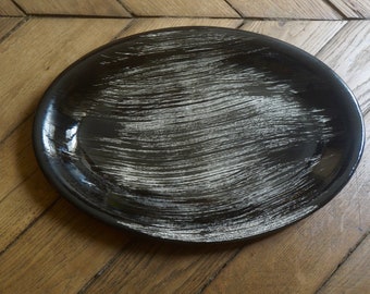 May include: A black oval ceramic serving platter with a white brushed finish. The platter has a smooth, glossy surface and is perfect for serving appetizers, desserts, or other dishes.