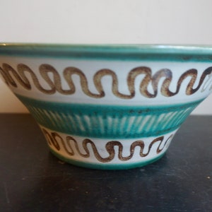 May include: A white ceramic bowl with a green and brown geometric pattern. The bowl has a wide rim and a rounded bottom.