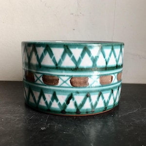 May include: A ceramic planter with a green and white geometric pattern. The planter has a brown band with brown dots around the middle.