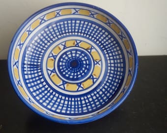May include: A blue and yellow ceramic bowl with a geometric pattern. The bowl has a white background with blue and yellow lines and circles.