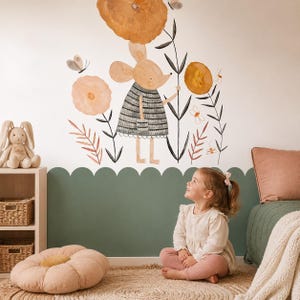 May include: A wall decal featuring a watercolour illustration of a mouse wearing a grey striped dress, surrounded by large orange flowers, thin black stems, and small butterflies. The design is applied to a white wall above a sage green scalloped border.