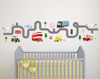 May include: A colorful road with traffic signs and various vehicles, including a police car, a red double-decker bus, a fire truck, a tractor, a blue truck, and a yellow ambulance. The road is on a white wall with a gray crib in the foreground.