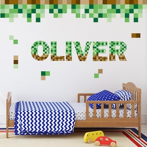 Könnte beinhalten: Kinderzimmer mit Holzbett und blau-weißer Bettwäsche. Der Name "OLIVER" ist in pixeligen grünen und braunen Buchstaben an der Wand zu sehen. Dekorativer grüner Pixelrand oben. Zwei Spielzeugautos am Fuß des Bettes.