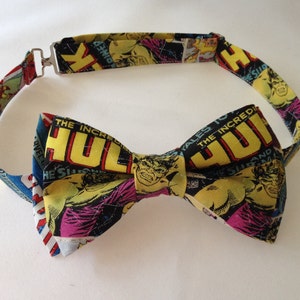 Puede incluir: Una pajarita con un diseño de cómic que presenta a Hulk. La pajarita tiene un fondo negro con detalles en amarillo, verde, rosa y azul. La cinta ajustable para el cuello tiene un cierre de metal plateado.