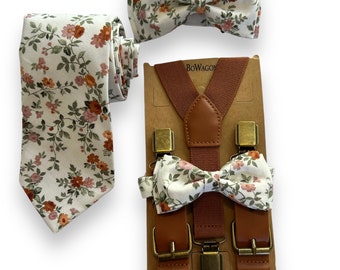 Puede incluir: Un conjunto de tirantes marrones con clips dorados, una corbata blanca con un patrón floral en tonos naranja y rosa, y dos pajaritas a juego. Las pajaritas y la corbata tienen un fondo blanco con un patrón floral en tonos naranja y rosa. Los tirantes tienen una correa de cuero marrón y clips dorados. El embalaje es marrón con la palabra "BOWAGON" impresa en él.