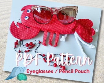 Puede incluir: Bolsa de tela con forma de langosta de lunares rojos y blancos con un par de gafas de sol marrones en su interior. La bolsa está sobre un fondo azul claro con arena blanca y una concha. El texto "PDF Pattern Eyeglasses / Pencil Pouch" está debajo de la bolsa.