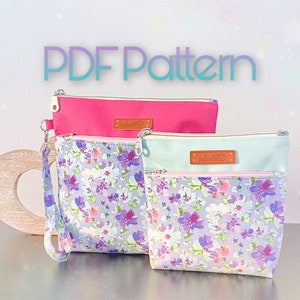 May include: Two zippered pouches with floral patterns. The top pouch is pink and the bottom pouch is light blue with a white floral pattern. Both pouches have a brown leather tag with the text "made with love".