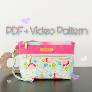 May include: A pink and blue zippered pouch with a floral print and a gold zipper. The pouch has a pink fabric flap with a gold zipper and a small label that says "Made With Love".