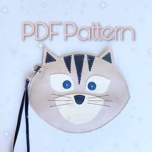May include: A PDF pattern for a cute cat-shaped coin purse. The purse is made of faux leather and has a black strap.