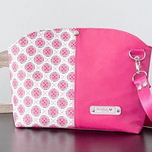 May include: A pink and white patterned cosmetic bag with a pink strap and a silver clasp. The bag has a label that says "Hand Made with Love".
