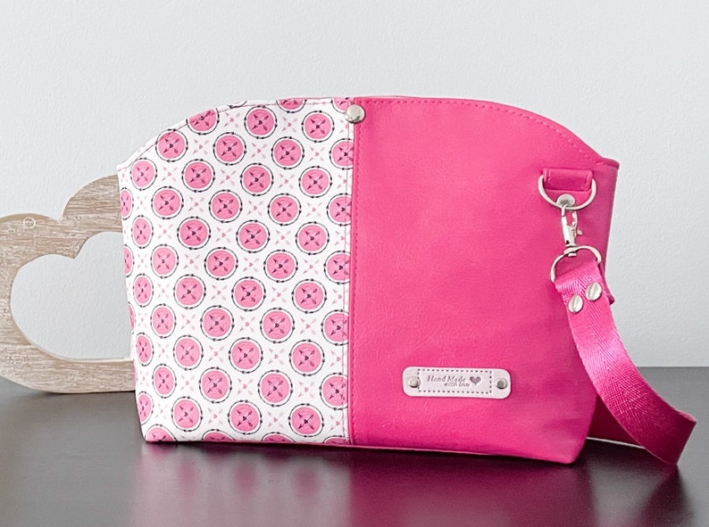 May include: A pink and white patterned cosmetic bag with a pink strap and a silver clasp. The bag has a label that says "Hand Made with Love".