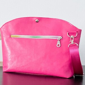 May include: A bright pink crossbody bag with a silver zipper and a silver clasp. The bag has a short strap and a long adjustable strap.