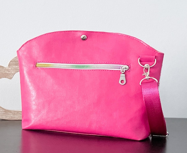 May include: A bright pink crossbody bag with a silver zipper and a silver clasp. The bag has a short strap and a long adjustable strap.