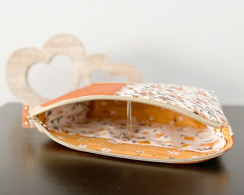 May include: A small, zippered pouch with a floral print on one side and a solid orange fabric on the other. The pouch is open and the inside is lined with a yellow floral fabric.
