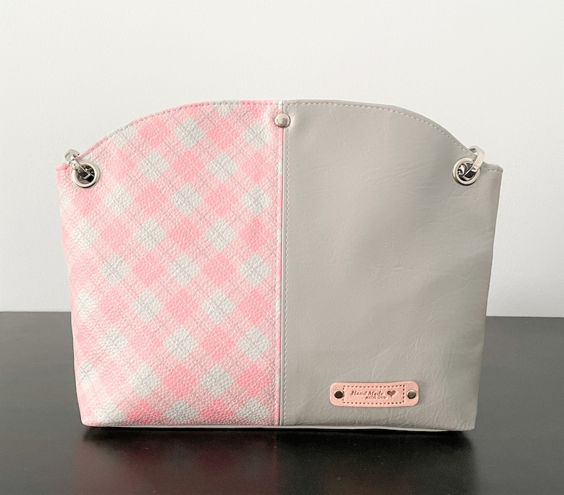 May include: A gray and pink checkered handbag with a silver chain strap and a small leather tag that says "Hand Made with Love".