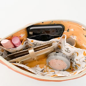 May include: An orange zippered pouch with a floral print lining. The pouch is open and contains a phone, wallet, makeup, and other small items.